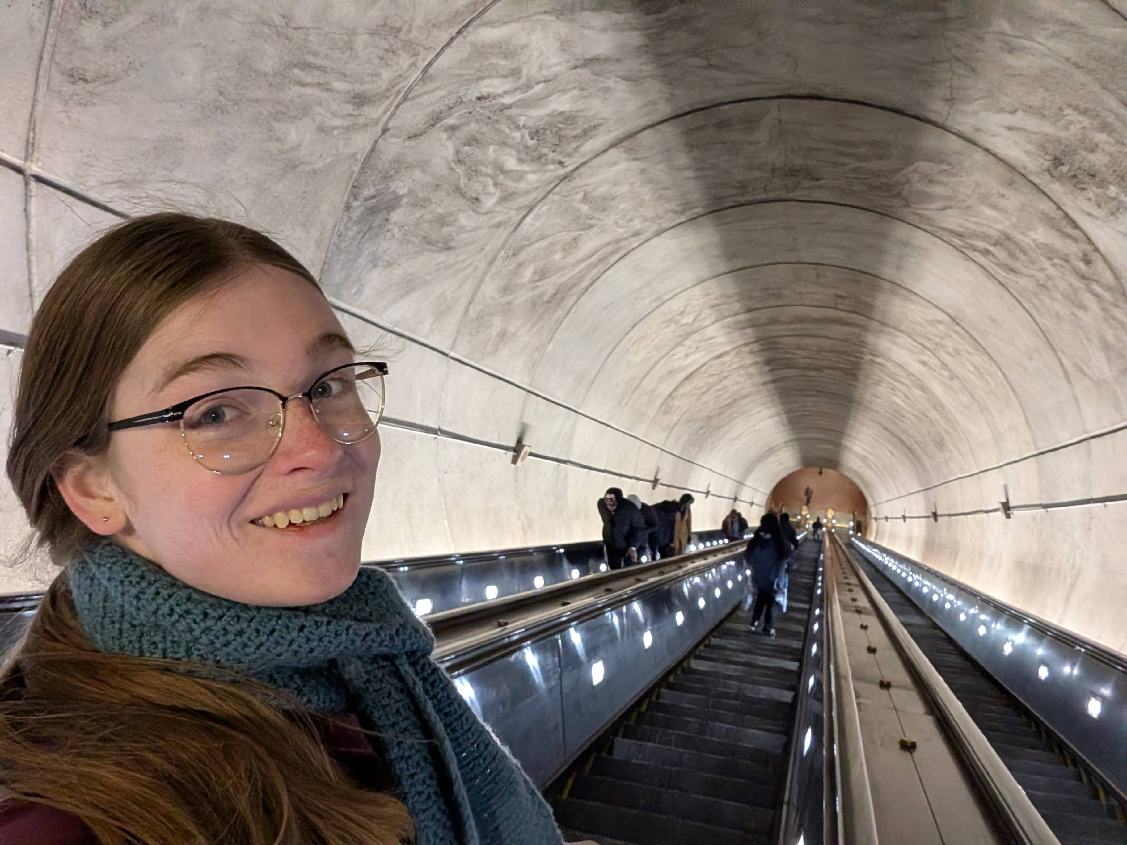 A person with glasses smiling on an escalator